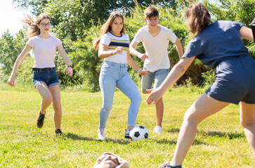 Obraz premium Company of glad teenagers playing football in park