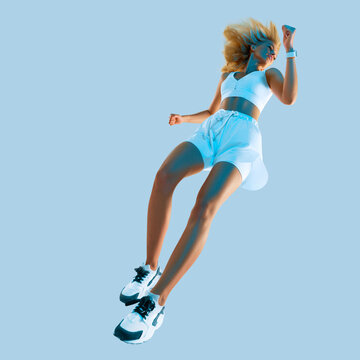 Profile picture of inspired energetic caucasian female in sportswear running and jumping, isolated along gray background. Motivation fitness concept studio photo. Creative blue light
