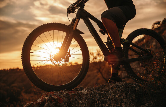 Crop man riding bicycle at sunset