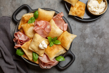 Top view of Italian  appetizer. Fried bread crescentine or gnocco fritto with mortadella and soft cheese, decorated with basil leaves. Traditional food. - obrazy, fototapety, plakaty