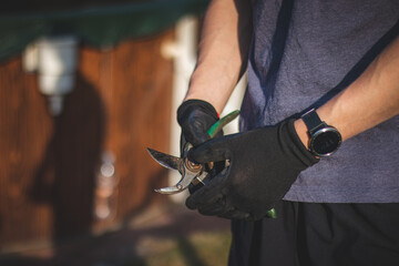 Detail of a middle-aged man's hand and the black glove in which he holds his work tool - a pair of loppers. Watch showing physical activity