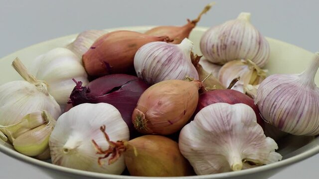 Close rotating shot of onions, shallots and garlic in white bowl