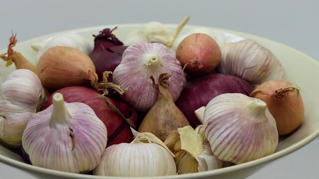 Spinning close-up of many onions, garlic and shallots in round bowl