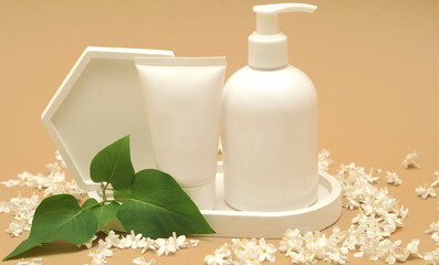 White cosmetic bottles with lilac on background. Scrub, gel shower and cream on light background with lilac petals.
