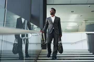 Full length portrait of successful African-American businessman walking down stairs in office building and looking away, copy space