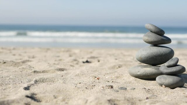 Rock balancing on ocean beach, stones stacking by sea water waves. Pyramid of pebbles on sandy shore. Stable pile or heap in soft focus with bokeh, close up. Zen balance, minimalism, harmony and peace