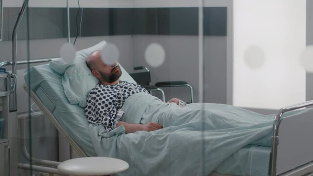 Sick man resting in bed wearing nasal oygen tube waiting practitioner doctor for disease examination after medical surgery in hospital ward. Hospitalized patient having respiratory disorder