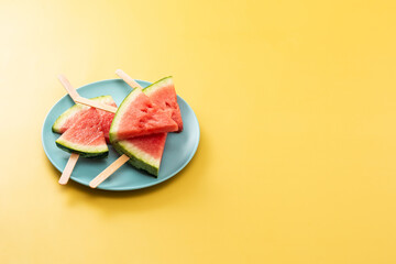 Watermelon slices popsicles on blue plate and yellow background. Copy space