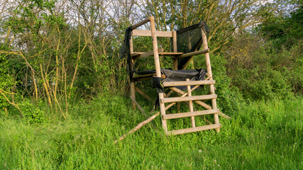 Lookout wooden ladder seat, also known as hunter's seat, hunter's high seat between the trees in nature for observing wild animals, animal world covered with camouflage hunting camouflage net