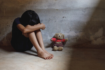 Girl shouts covered her face sitting alone on floor with her bear in dark room. concept for...