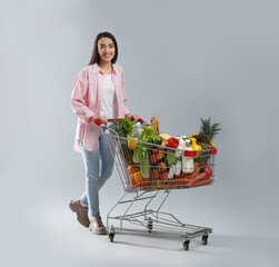 Young woman with shopping cart full of groceries on grey background © New Africa
