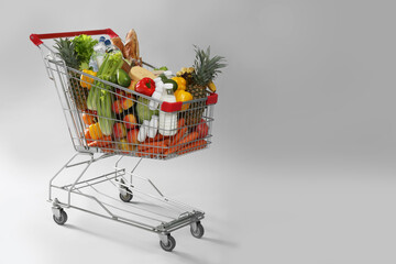 Shopping cart full of groceries on grey background. Space for text