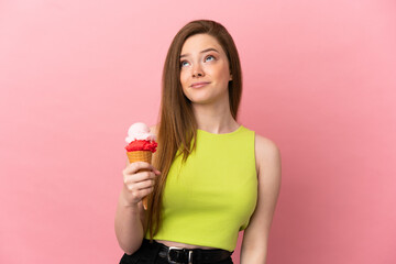 Teenager girl with a cornet ice cream over isolated pink background and looking up