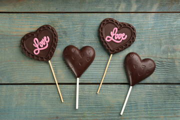 Different chocolate heart shaped lollipops on light blue wooden table, flat lay