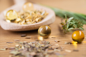 Fototapeta na wymiar Flaxseed oil capsules lie on a wooden table next to dry herbs and a wooden spoon.