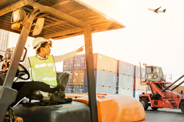African-American engineering woman supervises field work on forklifts by directing shipping work,...