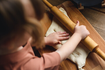 Close-up of a little girl's hand rolling out the dough. Mother teaches preschool girl to cook baked...