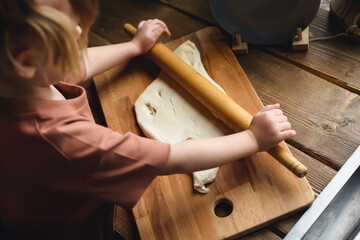Close-up of a little girl's hand rolling out the dough. Mother teaches preschool girl to cook baked goods