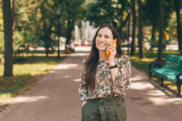 Portrait of cheerful young business woman outdoors in park talking on smartphone