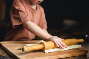 Close-up of a little girl's hand rolling out the dough. Mother teaches preschool girl to cook baked goods