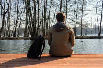Man sits alone on a pier by the lake and thinking after hiking. Amazing nature view with lake and...