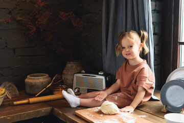 A little girl sits at the kitchen table and sculpts from dough. Mom and Daughter Cook Together
