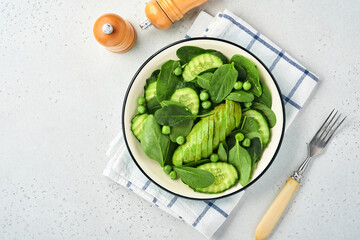 Green vegetable salad with spinach, avocado, green peas and olive oil in bowl on light gray slate,...