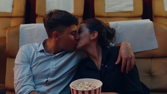 Attractive cheerful young caucasian couple kissing romantic moment while watching film in movie theater. Lifestyle entertainment concept.