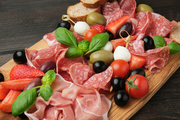 Salami prosciutto parma ham serving with olives strawberries on wooden board