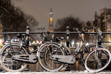 Winter cityscape with night view of snowy covered bicycles parked on canal bridge, Blurred...