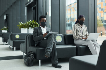 Graphic full length portrait of two business people wearing masks while working in waiting lounge...