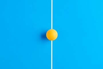 Yellow table tennis ball on the line of a ping pong table.