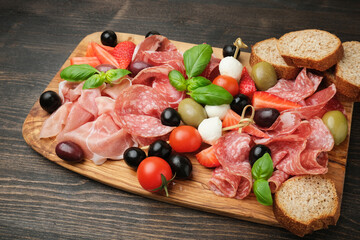 Salami prosciutto parma ham serving with olives strawberries on wooden board
