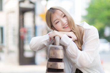 Asian beautiful woman with bronze hair  in white shirt while sits happy smilie on the edge of a...
