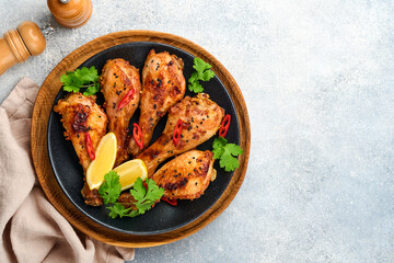 Grilled chicken drumsticks or legs or roasted bbq with spices and tomato salsa sauce on a black plate on light grey slate, stone or concrete background. Top view with copy space.