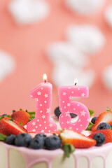 Birthday cake number 15. Beautiful pink candle in cake on pink background with white clouds. Close-up and vertical view