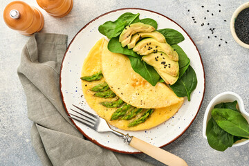 Omelette or omelet stuffed with asparagus, avocado and spinach leaves for breakfast on white plate over white slate, stone or concrete background. Balanced and tasty morning food. Mock up. Top view.