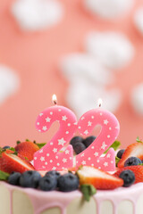 Birthday cake number 22. Beautiful pink candle in cake on pink background with white clouds. Close-up and vertical view