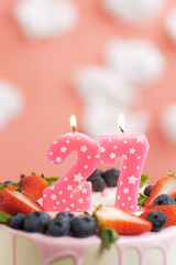 Birthday cake number 27. Beautiful pink candle in cake on pink background with white clouds. Close-up and vertical view