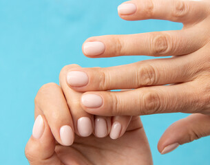 manicure in light tone gel polish on hands on a blue background