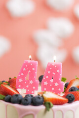 Birthday cake number 44. Beautiful pink candle in cake on pink background with white clouds. Close-up and vertical view