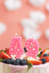 Birthday cake number 49. Beautiful pink candle in cake on pink background with white clouds. Close-up and vertical view