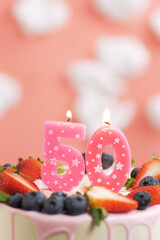 Birthday cake number 50. Beautiful pink candle in cake on pink background with white clouds. Close-up and vertical view