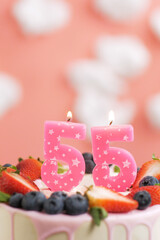Birthday cake number 55. Beautiful pink candle in cake on pink background with white clouds. Close-up and vertical view
