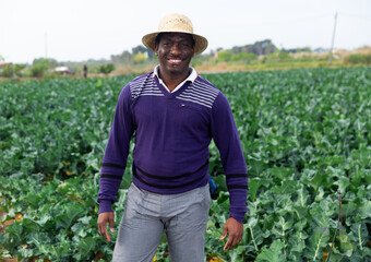 Portrait of smiling afro american man farmer in straw hat standing in farm field on sunny spring day