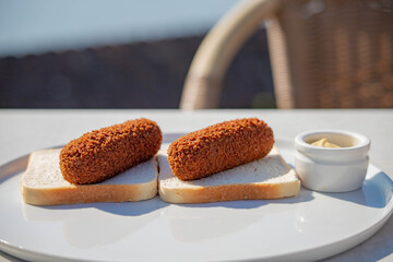 Broodje kroket (bread with a croquette) Dutch's favourite snack deep-fried ragout filled snack coated with breadcrumbs, Served with mustard on white plate.