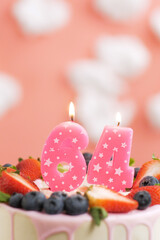 Birthday cake number 64. Beautiful pink candle in cake on pink background with white clouds. Close-up and vertical view