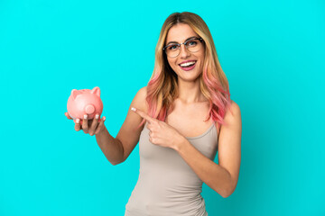 Young woman over isolated blue background holding a piggybank and pointing it