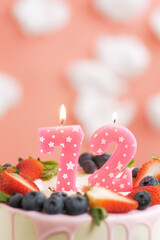 Birthday cake number 72. Beautiful pink candle in cake on pink background with white clouds. Close-up and vertical view