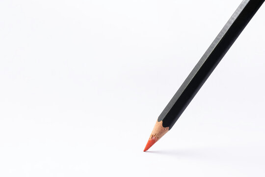 Black colored pencil with sharp red point stands on white paper. Background image